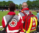 Foto: Zwei DRK-Sanitäter - von hinten zu sehen - stehen am Fußballfeld